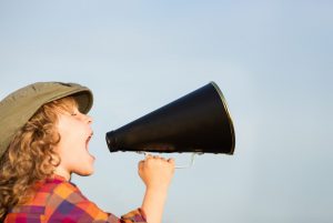 Kid shouting through vintage megaphone. Communication concept. Blue sky background as copy space for your text