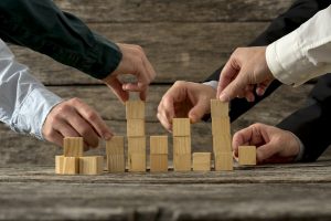 Hands of five businessman holding wooden blocks placing them into a structure. Conceptual of teamwork, strategy and business start up.