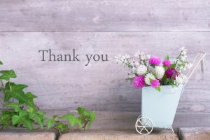 There Aru's in flower arrangement is placed on the back written on wooden wall and thank you