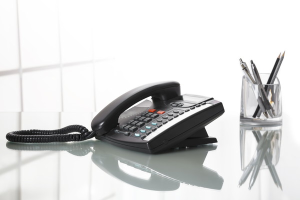 Close up of black landline phone on an office desk with white background