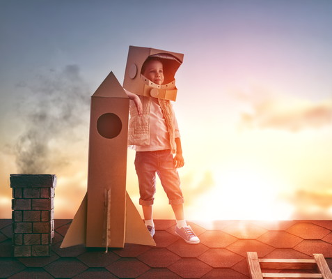 Little child boy plays astronaut. Child on the background of sunset sky. Child boy in an astronaut costume standing on the roof of the house and looking at the sky and dreaming of becoming a spaceman.