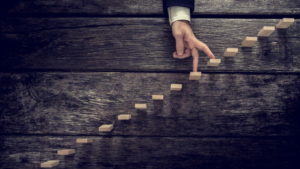 Retro image of a businessman walking his fingers up wooden steps mounted in rustic wooden boards towards light in a conceptual image of personal development, growth and success.