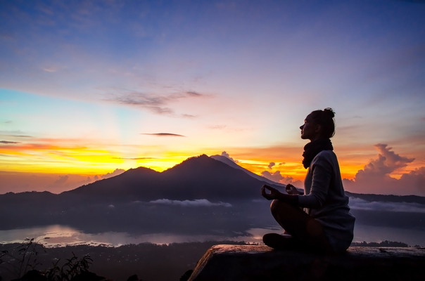 Silhouette of a girl that does yoga and meditation in the mountains at dawn. Stock image.