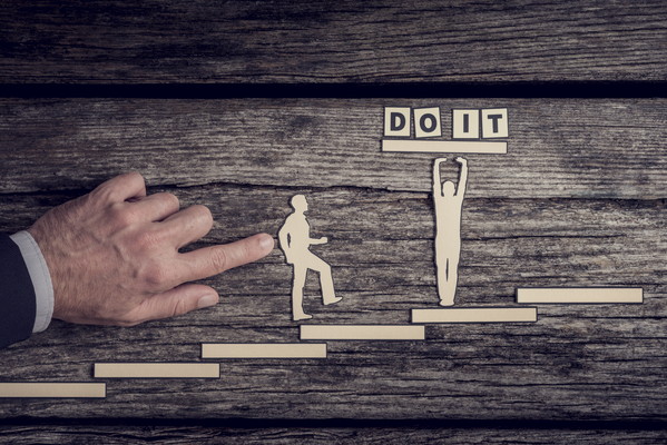 Hand of person pushing figures up stairs to do it sign with letter tiles, wooden background.